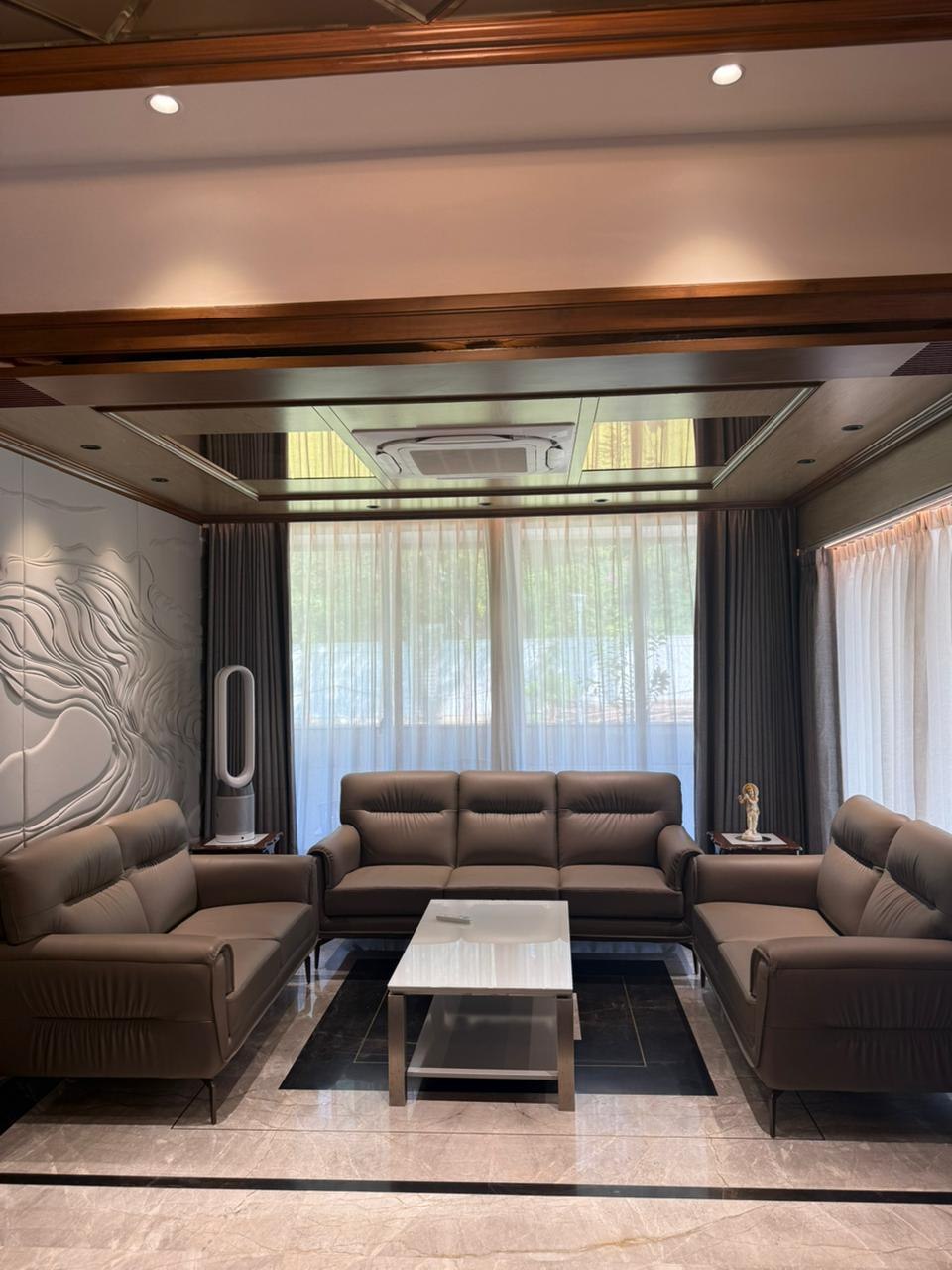 Living room with wood-beamed ceiling, sculptural stone feature wall, and three-piece leather sofa set